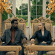 A man and a woman sit on ornate chairs in an opulant room.